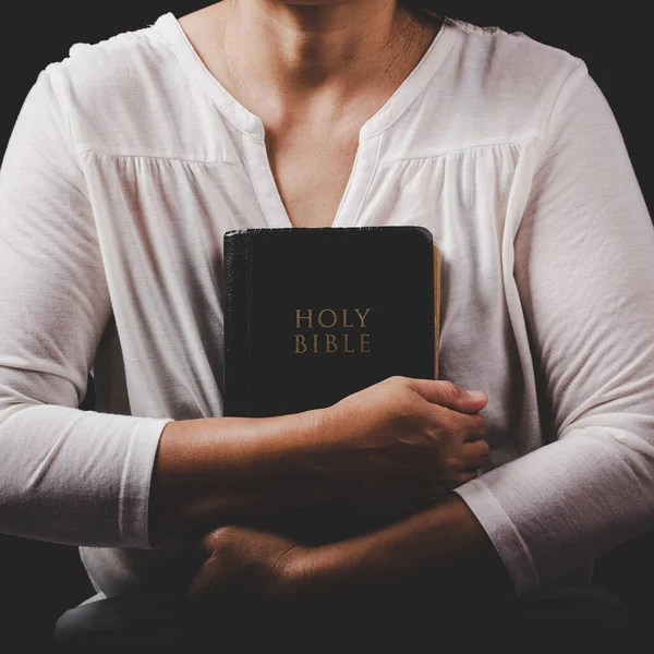 christian woman hand on holy bible are pray and worship for thank god in church with black background, adult female person are reading book, concept for faith, spirituality and religion