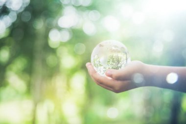 Human hands holding earth sphere crystal or sustainable globe glass with sunlight at green nature background in ecology environment forest. concept of conservation environmental, protection planet.