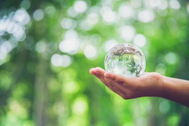 Human hands holding earth sphere crystal or sustainable globe glass with sunlight at green nature background in ecology environment forest. concept of conservation environmental, protection planet.