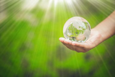 Human hands holding earth sphere crystal or sustainable globe glass with sunlight at green nature background in ecology environment forest. concept of conservation environmental, protection planet.