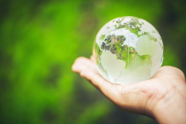 Human hands holding earth sphere crystal or sustainable globe glass with sunlight at green nature background in ecology environment forest. concept of conservation environmental, protection planet.