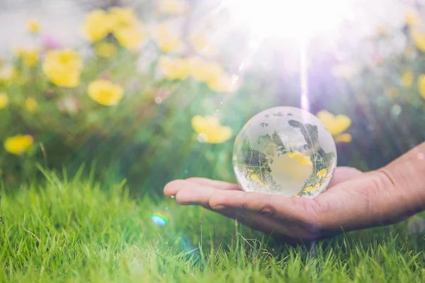 Human hands holding earth sphere crystal or sustainable globe glass with sunlight at green nature background in ecology environment forest. concept of conservation environmental, protection planet.