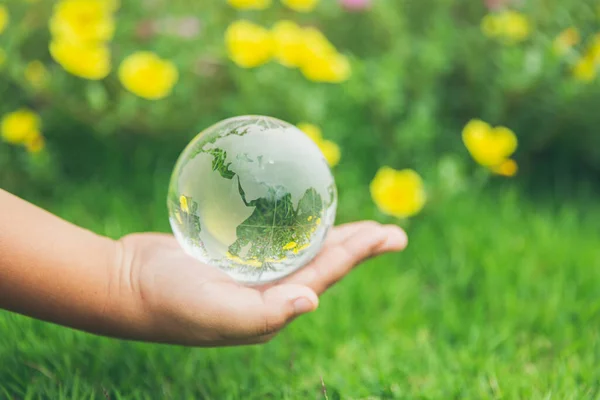 Human hands holding earth sphere crystal or sustainable globe glass with sunlight at green nature background in ecology environment forest. concept of conservation environmental, protection planet.