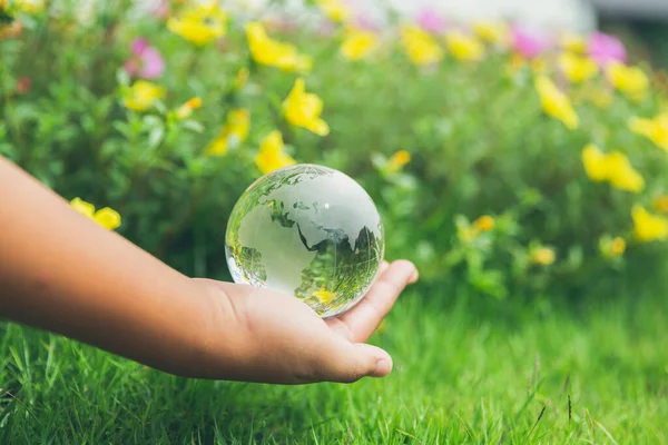 Human hands holding earth sphere crystal or sustainable globe glass with sunlight at green nature background in ecology environment forest. concept of conservation environmental, protection planet.