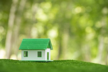 Environmentally eco-friendly real estate house. Small model building property home on grass in green nature ecology. Sustainable energy conservation residential design and sell - rent business concept