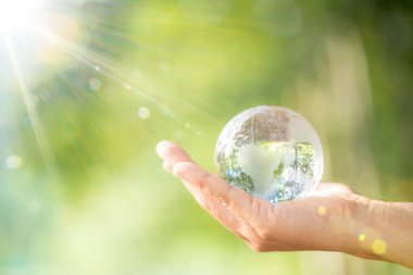 Human hand holding globe planet glass In green forest with bokeh nature lights. world environment day. concept for environment conservation, protect ecology earth and environmental eco-friendly life.