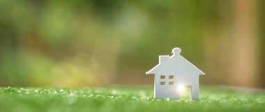 Environmentally eco-friendly real estate house. Small model building property home on grass in green nature ecology. Sustainable energy conservation residential design and sell - rent business concept