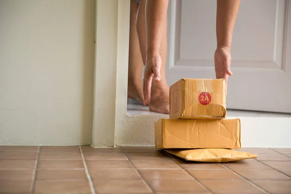 Woman collects parcel at door. box near door on floor. Online shopping, boxes delivered to your front door. Easy to steal when nobody is home. Parcel in cardboard box on doorstep. Delivery service