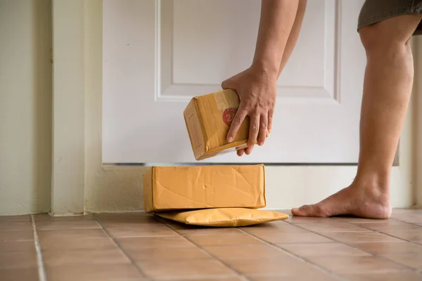 Woman collects parcel at door. box near door on floor. Online shopping, boxes delivered to your front door. Easy to steal when nobody is home. Parcel in cardboard box on doorstep. Delivery service