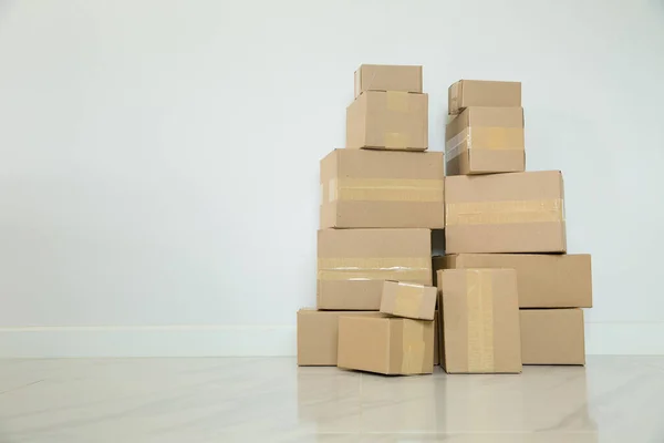 Stack of cardboard boxes for moving, Empty room with a white wall and cardboard boxes with unbranded barcode on the floor. Delivery of goods, shopping. Cardboard boxes on gray wall background.