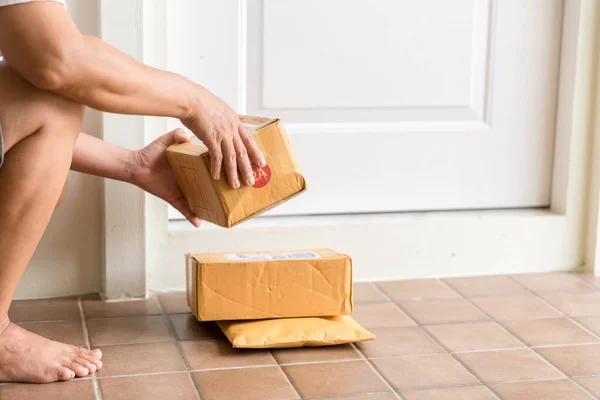 Woman collects parcel at door. box near door on floor. Online shopping, boxes delivered to your front door. Easy to steal when nobody is home. Parcel in cardboard box on doorstep. Delivery service