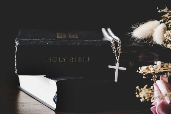 Holy bible book with cross or crucifix on old black wooden background. Christian catholic with protestant pray and study in church. Concept of cognition about faith god and religion, jesus spiritual.