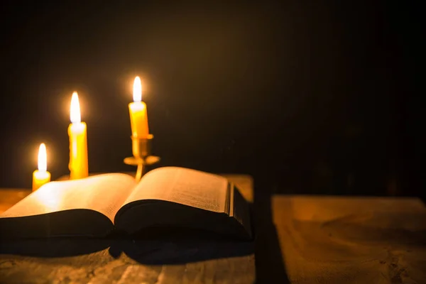 用圣经上的点燃的蜡烛和十字架或十字架钉在教堂古老的木制背景上 烛光和打开的旧式木桌书 家庭中的基督教学习和阅读 基督宗教的概念 — 图库照片