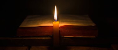 Kilisedeki eski ahşap zemin üzerinde kutsal İncil ve haç olan mum ışığı. Mum ışığı ve klasik ahşap masa hristiyanlığı çalışmaları ve evde okuma üzerine açık kitap. Hristiyan dini kavramı.