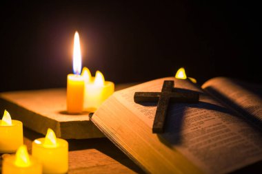 Kilisedeki eski ahşap zemin üzerinde kutsal İncil ve haç olan mum ışığı. Mum ışığı ve klasik ahşap masa hristiyanlığı çalışmaları ve evde okuma üzerine açık kitap. Hristiyan dini kavramı.