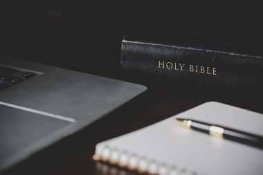 Siyah ahşap arka planda eğitim için kâğıt içeren kutsal İncil kitabı. Protestan inancı olan Hıristiyan Katolik kilisede dua ediyor. İnanç, Tanrı ve din hakkında bilgi edinme kavramı..
