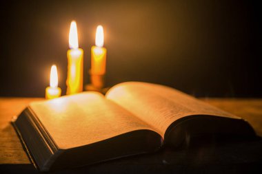 Kilisedeki eski ahşap zemin üzerinde kutsal İncil ve haç olan mum ışığı. Mum ışığı ve klasik ahşap masa hristiyanlığı çalışmaları ve evde okuma üzerine açık kitap. Hristiyan dini kavramı.
