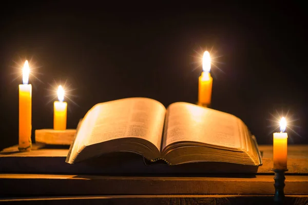 Light candle with holy bible and cross or crucifix on old wooden background in church.Candlelight and open book on vintage wood table christianity study and reading in home.Concept of christ religion