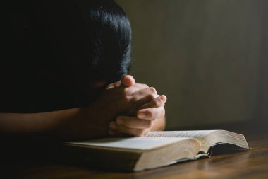 Dua eden kişi siyah arka planda. Hıristiyan katolik kadın kilisede karanlıkta Tanrı 'ya dua ediyor. Kız İsa 'ya inanıyor ve inanıyor. İsa dini ve Hıristiyanlık ibadeti veya dua kavramı.