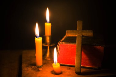 Kilisedeki eski ahşap zemin üzerinde kutsal İncil ve haç olan mum ışığı. Mum ışığı ve klasik ahşap masa hristiyanlığı çalışmaları ve evde okuma üzerine açık kitap. Hristiyan dini kavramı.