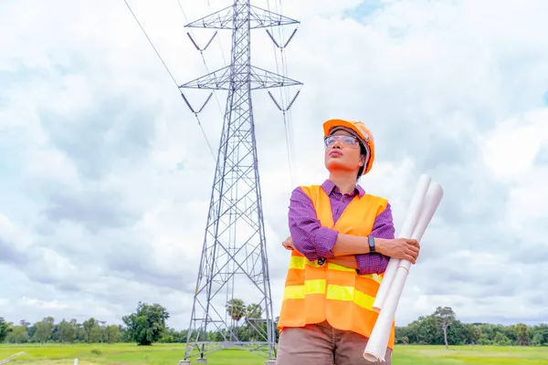 Kadın mühendis inşaat işçisi dijital ipad ya da bilgisayarda düzeni kontrol ediyor. Foreman elektrik kulesi arka planında inşaat alanında çalışıyor..