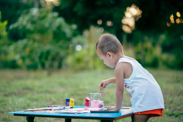子供の絵 汚れた手と指で幸せな小さなかわいい子供の女の子は 紙や彼女のタンクの上に絵筆の絵を使用しています 裏庭の庭で水の色を描く小さな女の子 — ストック写真