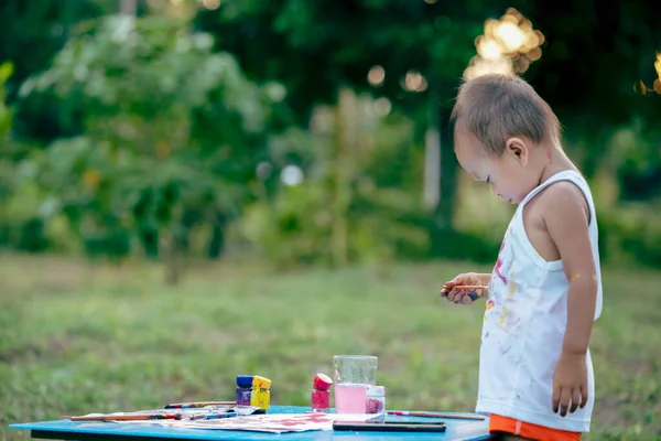 Çocuk boyama. Kirli elleri ve parmakları olan mutlu küçük kız çocuğu, boya fırçasını kağıt ve kolsuz bluzuyla boyuyor. Bahçede sulu boya yapan küçük bir kız..