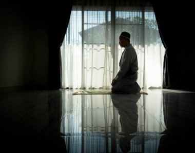 Evdeki oturma odasında dua eden Müslüman bir adam. Din Görev Günlüğü. İnsanların silueti