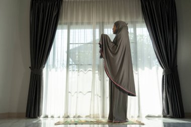 Evdeki oturma odasında dua eden Müslüman bir kadın. Din Görev Günlüğü. İnsanların silueti