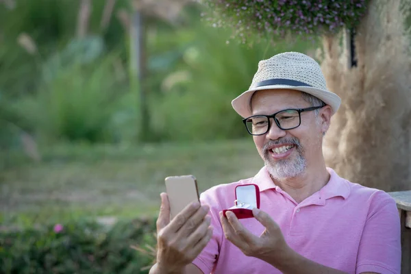 Mutluluk Adamı internetten kız arkadaşına dizüstü bilgisayarla sürpriz evlilik teklifi yapıyor. Gri sakallı emeklilik ya da Sunset 'teki yaşlı adam. Karantina Sevgililer Günü konsepti.