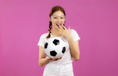 İzole edilmiş pembe arka planda beyaz tişörtlü Asyalı genç kadın elinde futbol topu, futbol konsepti