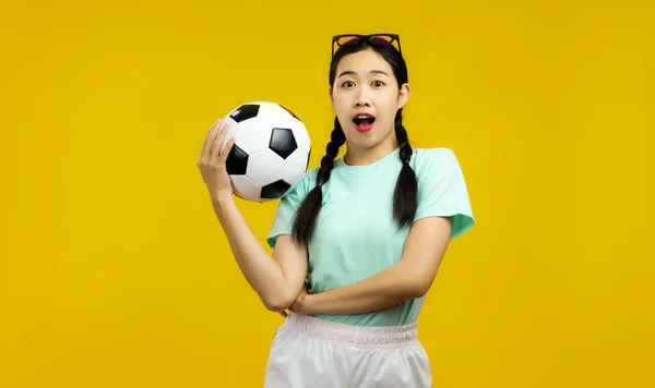 Zaskoczony Azji Młoda Kobieta Odizolowanym Żółtym Tle Trzyma Piłkę Nożną — Zdjęcie stockowe