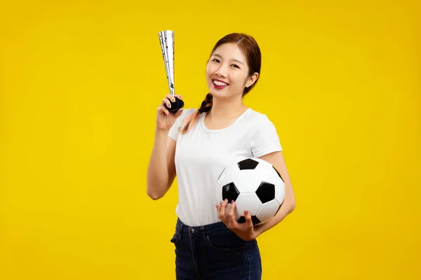 黄色の背景に孤立したサッカーボールと応援ホーンを保持する楽しいアジアの女性 スポーツの概念 — ストック写真