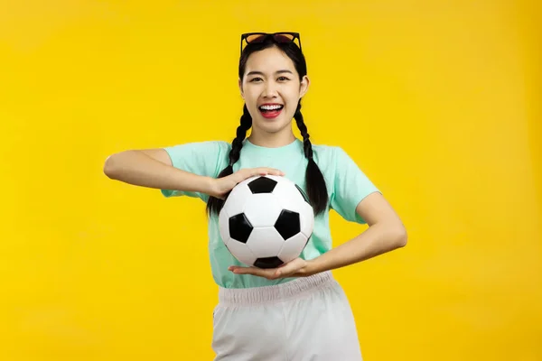 黄色の背景に孤立したサッカーボールを保持している陽気なアジアの女性の肖像 サッカースポーツの概念 — ストック写真