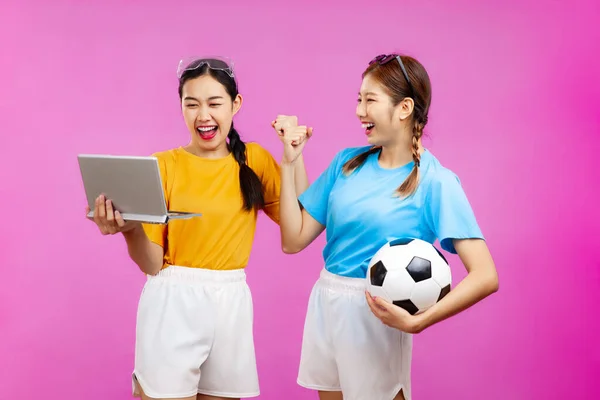 Két Vidám Ázsiai Izolált Rózsaszín Háttér Kezében Egy Focilabda Laptop — Stock Fotó