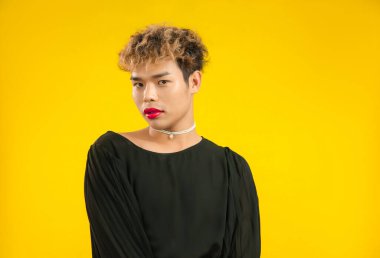 Sarı arka planda lgbtq ve lgbtq + pozu veren siyah gömlekli, kırmızı rujlu genç Asyalı bir adam..