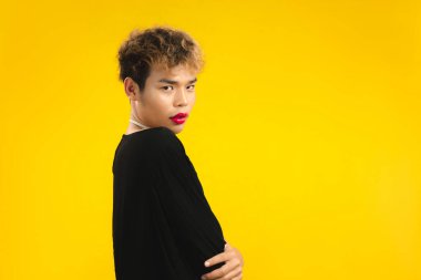 Sarı arka planda kırmızı rujlu, siyah gömlekli, kadınsı görünümlü Asyalı bir genç. lgbtq ve lgbtq + kavramı