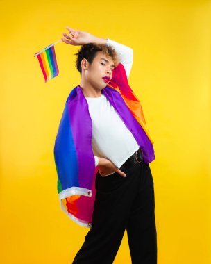 Omzunda LGBT Gökkuşağı bayrağı olan gururlu genç adam sarı arka plan izole edildi. Gay gururlu bir adam kameraya bakıyor..