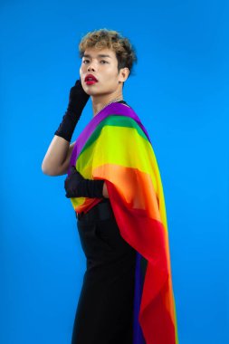 Makyajlı ve gururlu Asyalı eşcinsel Flaq, izole edilmiş mavi arka plan pozu veriyor. Transseksüel erkek LGBTQ + kavramları