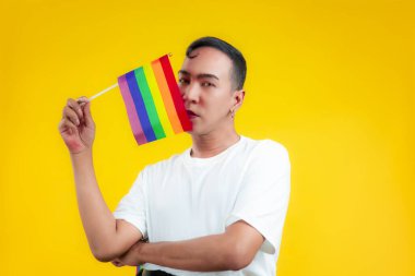 lgbt ve lgbtq + kavramının sarı arka planında lgbtq bayrağı tutan beyaz tişörtlü yakışıklı eşcinsel adam.