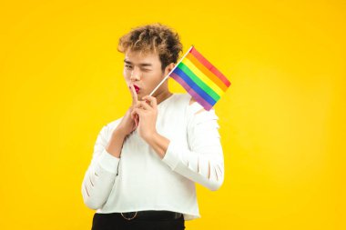 Beyaz tişörtlü yakışıklı Asyalı eşcinsel adam sarı arka planda duran Igbt gurur bayrağı taşıyor..
