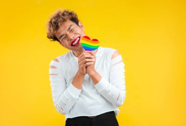 Elinde gökkuşağı kağıdı tutan mutlu Asyalı eşcinsel adam lgbtq ve lgbtq + kavramında kalbi kesti izole edilmiş sarı arkaplan pozu verdi.