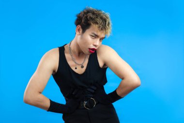 Kırmızı dudak nemlendiricisi ve siyah kolsuz gömlekli Asyalı gay adamın stüdyo portresi mavi arka planda. Transseksüel erkek LGBTQ + kavramları