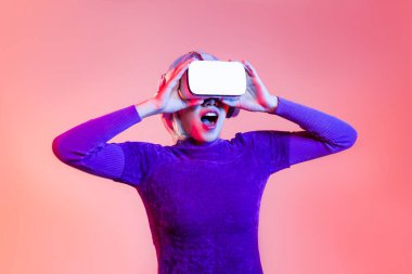 Metaverse konsept, mor tişörtlü Asyalı genç kadın siber punk saç stili VR kulaklık takıyor renkli arka planda dokunarak oynuyor..