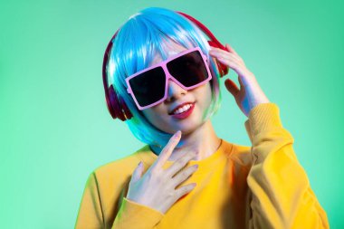 Dünyada müzik var. Neon yeşil arka planda izole edilmiş kulaklıklı genç Asyalı kadınlar. İnsani duygular, yüz ifadesi kavramı