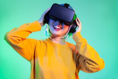 Metaverse konsept, sarı kazaklı mutlu Asyalı kadın VR kulaklık takıyor ve yeşil ekran arka planında oynuyor ve izliyor.