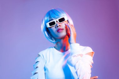 Young asian woman in white fashion crop sweatshirt wearing retro sunglasses posing dancing on the purple background in a Metaverse and cyborg concept.	