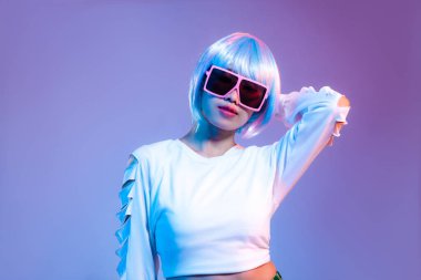 Beyaz moda hasat kazağı giyen Asyalı genç bir kadın. Metaevren ve cyborg konseptiyle mor duvarda duran güneş gözlüğü takıyor..