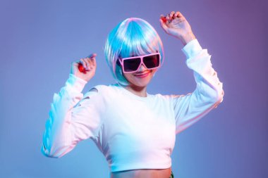 Metaverse ve cyborg konsepti. Eski güneş gözlüğü takan Asyalı genç bir kadın mor arka planda dans ediyor..