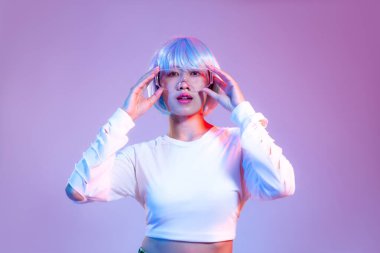 Metaverse ve cyborg konsepti. Mor arka planda güneş gözlüğü takan beyaz tarla kazağı giyen Asyalı genç kadın..